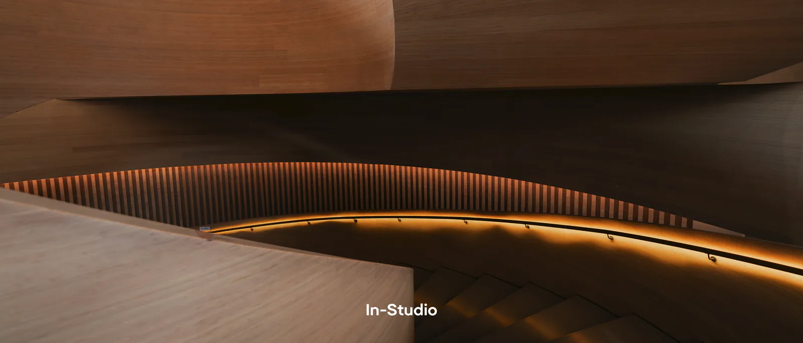 Escalier en bois courbe éclairé par une ligne lumineuse, avec le nom In-Studio