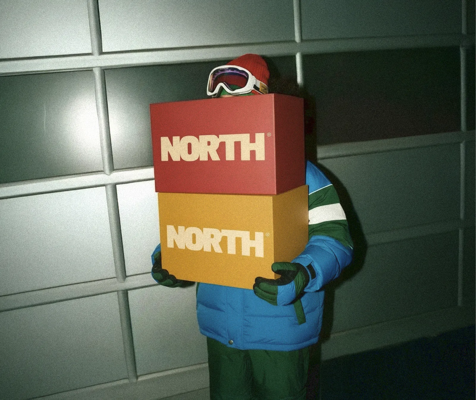 Personne en tenue de ski portant deux boîtes NORTH® rouge et jaune